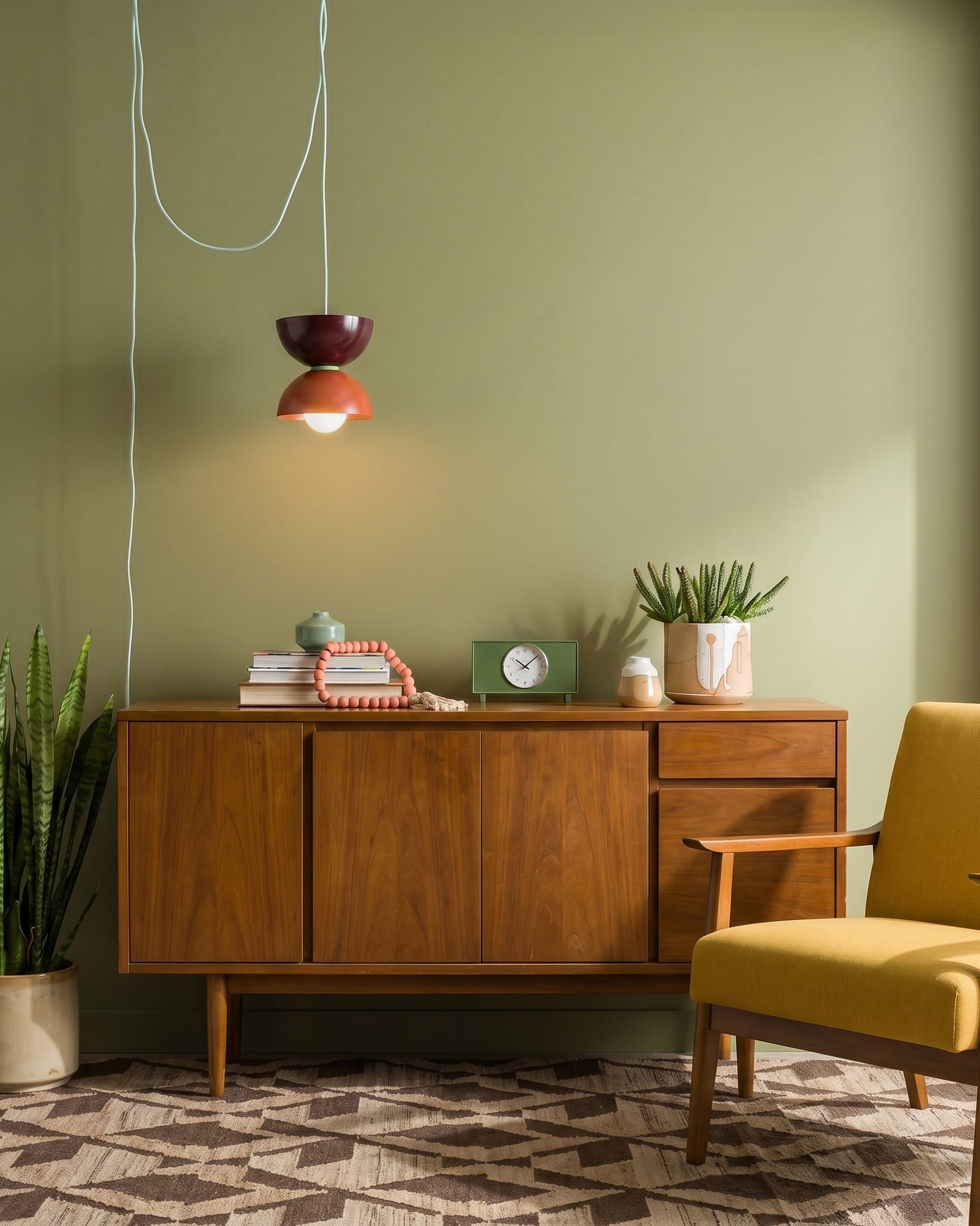 Mid century modern wood console with goldenrod colored chair. Chroma Studio Strata Mini Horizon plug-in pendant in rust, oxblood, and eucalyptus colors. 