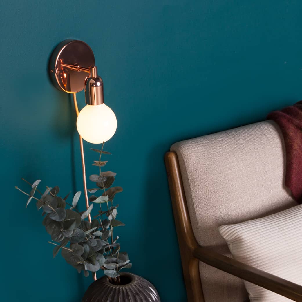 Junction Mini Solo Plug-In Sconce in Polished Copper finish. Mounted on aegean blue wall next to mid-century modern chair