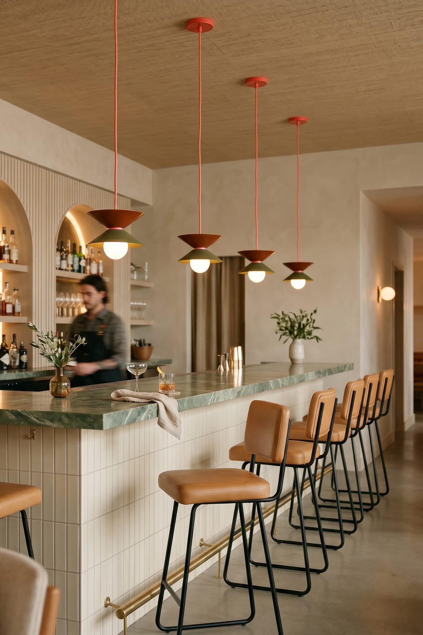 Modern kitchen with pendant lights, bar stools, and a person in the background.