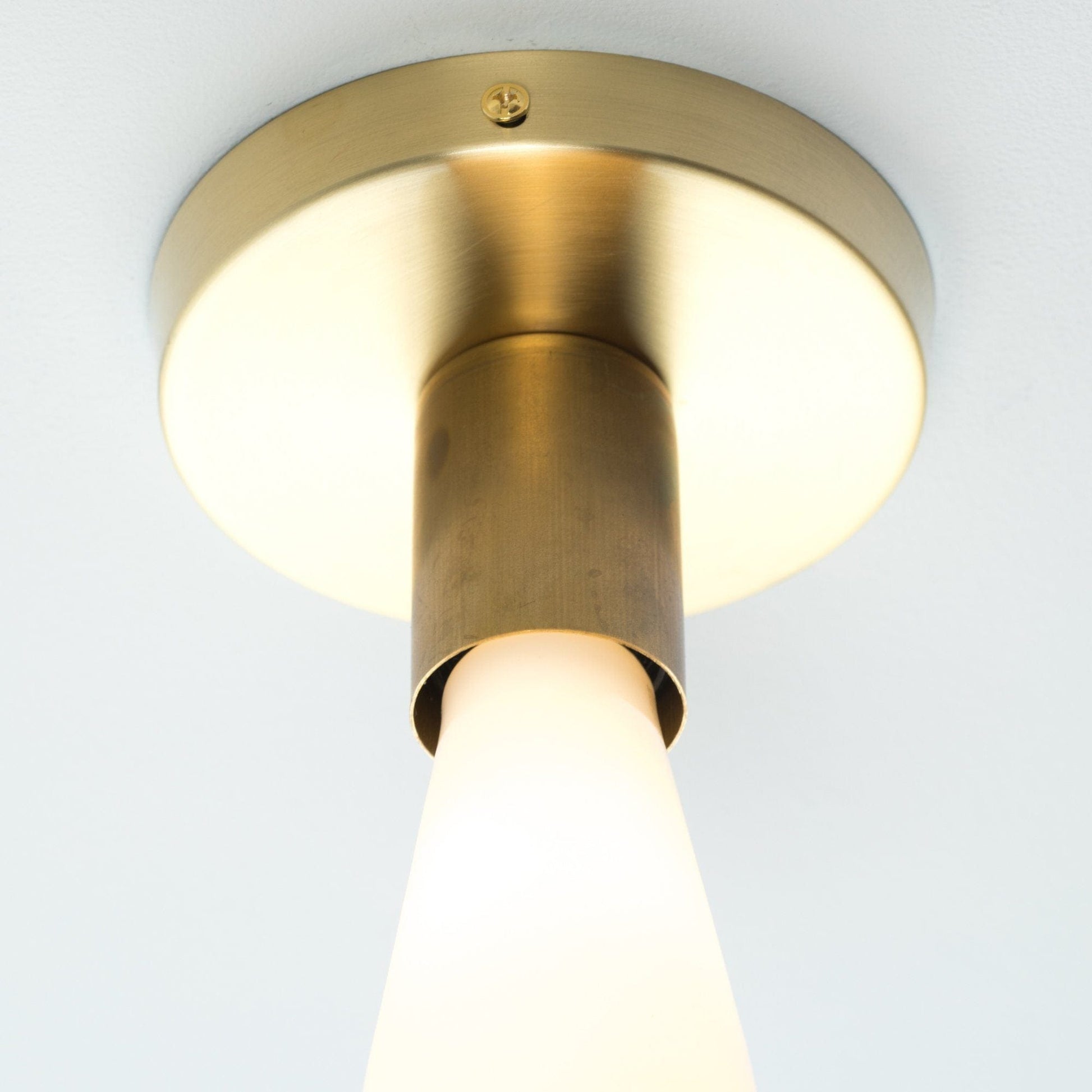 Close Up photo of Button Light in Raw Brass finish. Pictured with an Edison milk glass light bulb