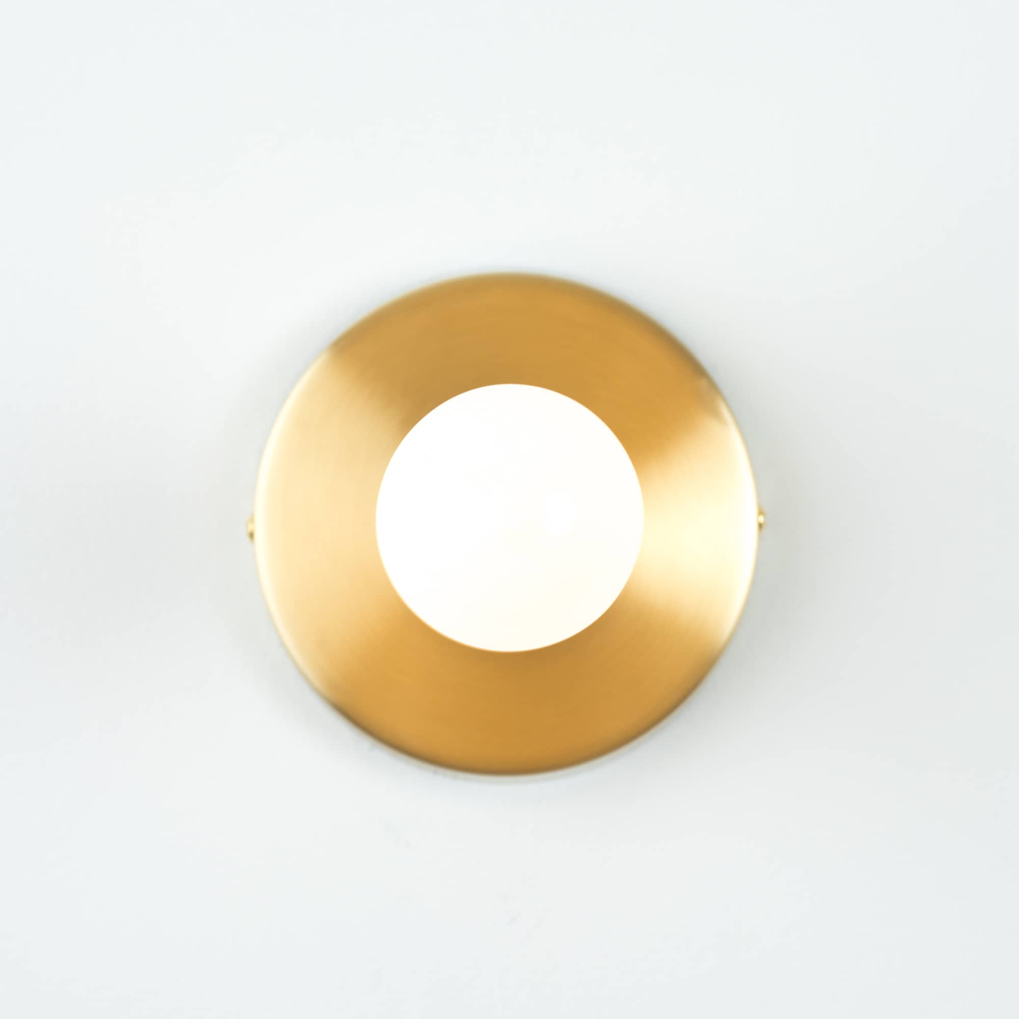 Button Light in Raw Brass finish. Pictured with a G25 milk glass light bulb. Straight on angle.