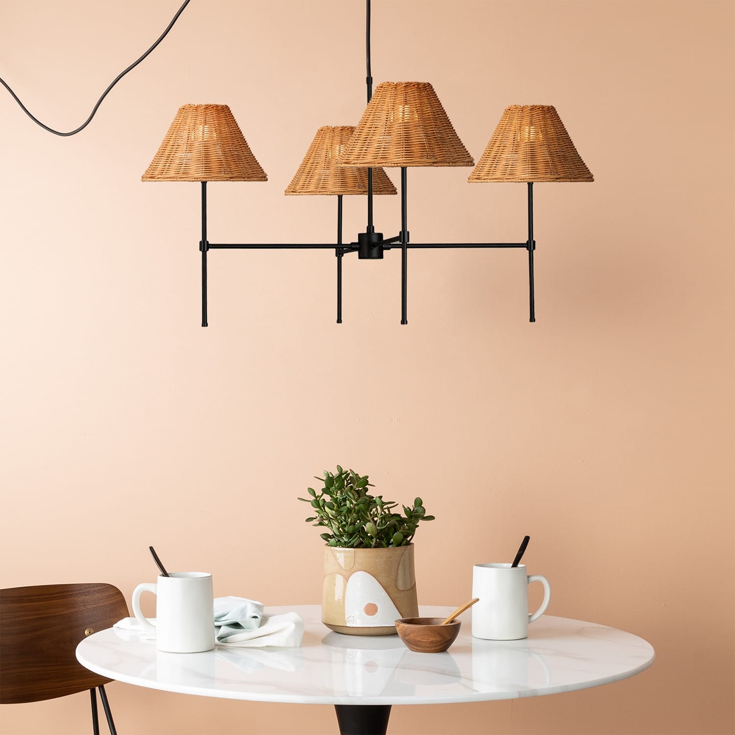 Modern chandelier with wicker shades over a dining table with mugs and a plant.