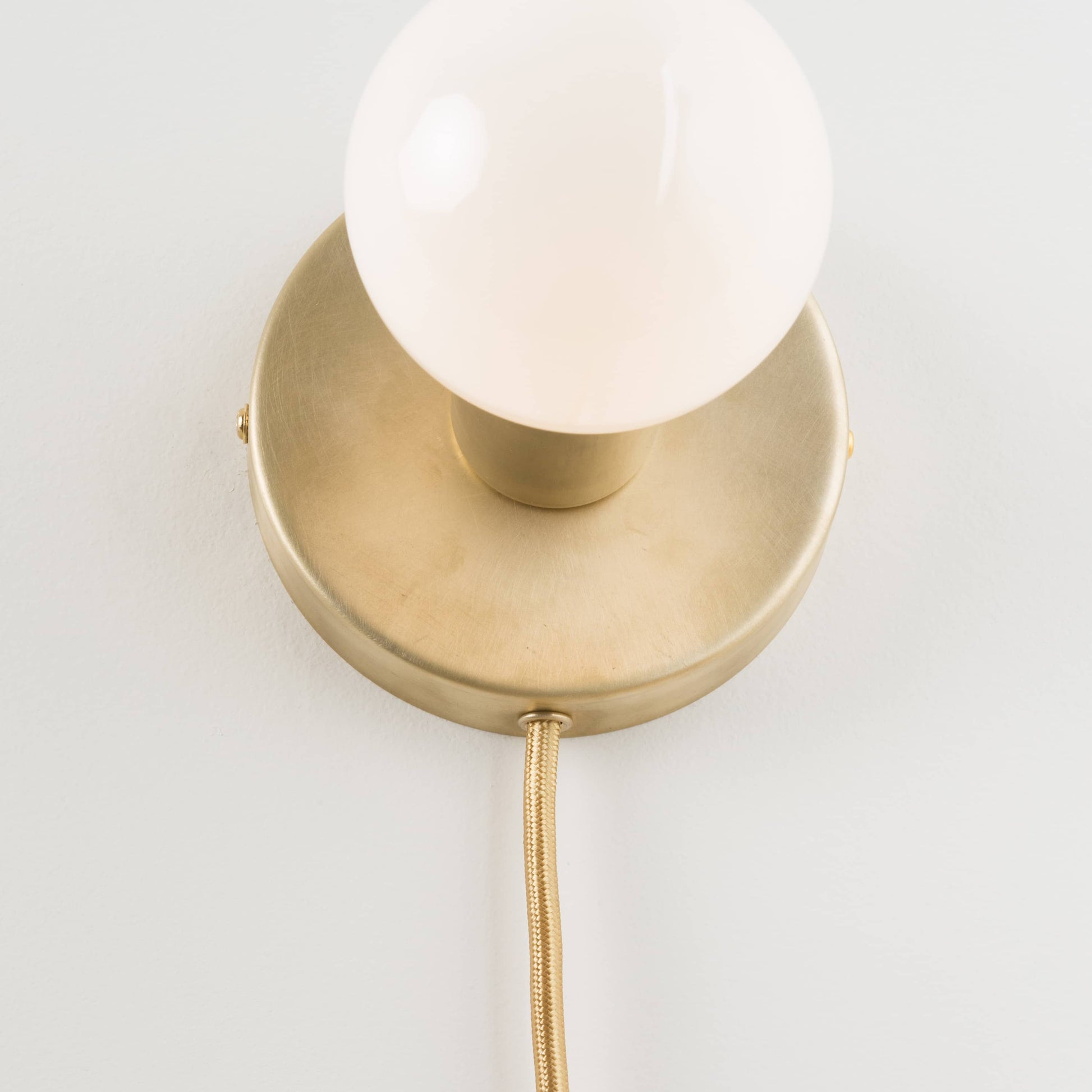 Close-up detail photo of Button Plug-In Sconce in Raw Brass finish with G40 bulb. 