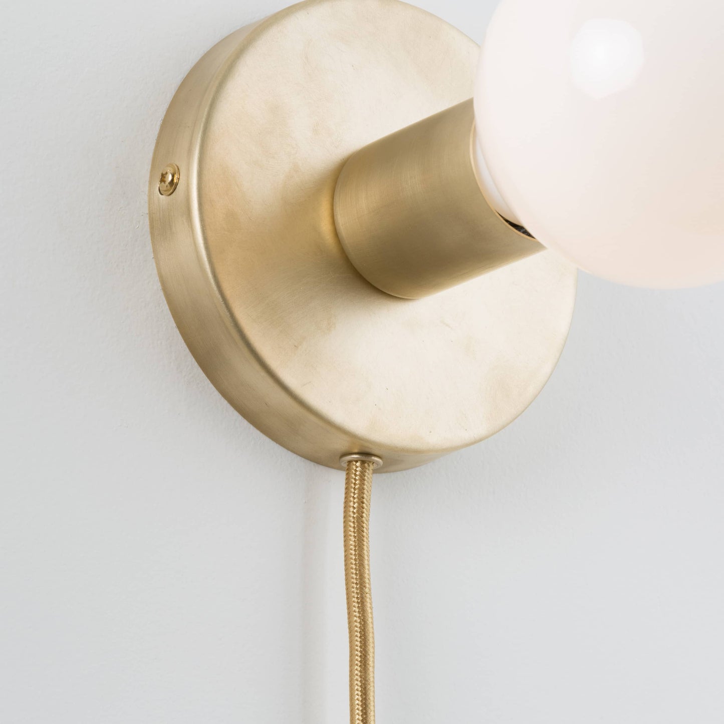Close-up detail photo of Button Plug-In Sconce in Raw Brass finish with G40 bulb. Power Cord is finished with an eyelette in the canopy 