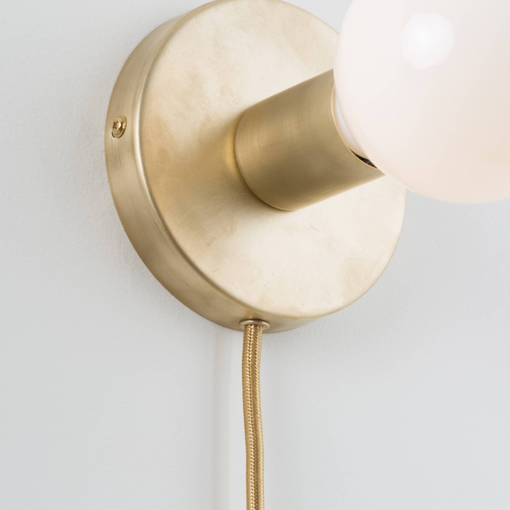 Close-up detail photo of Button Plug-In Sconce in Raw Brass finish with G40 bulb. Power Cord is finished with an eyelette in the canopy