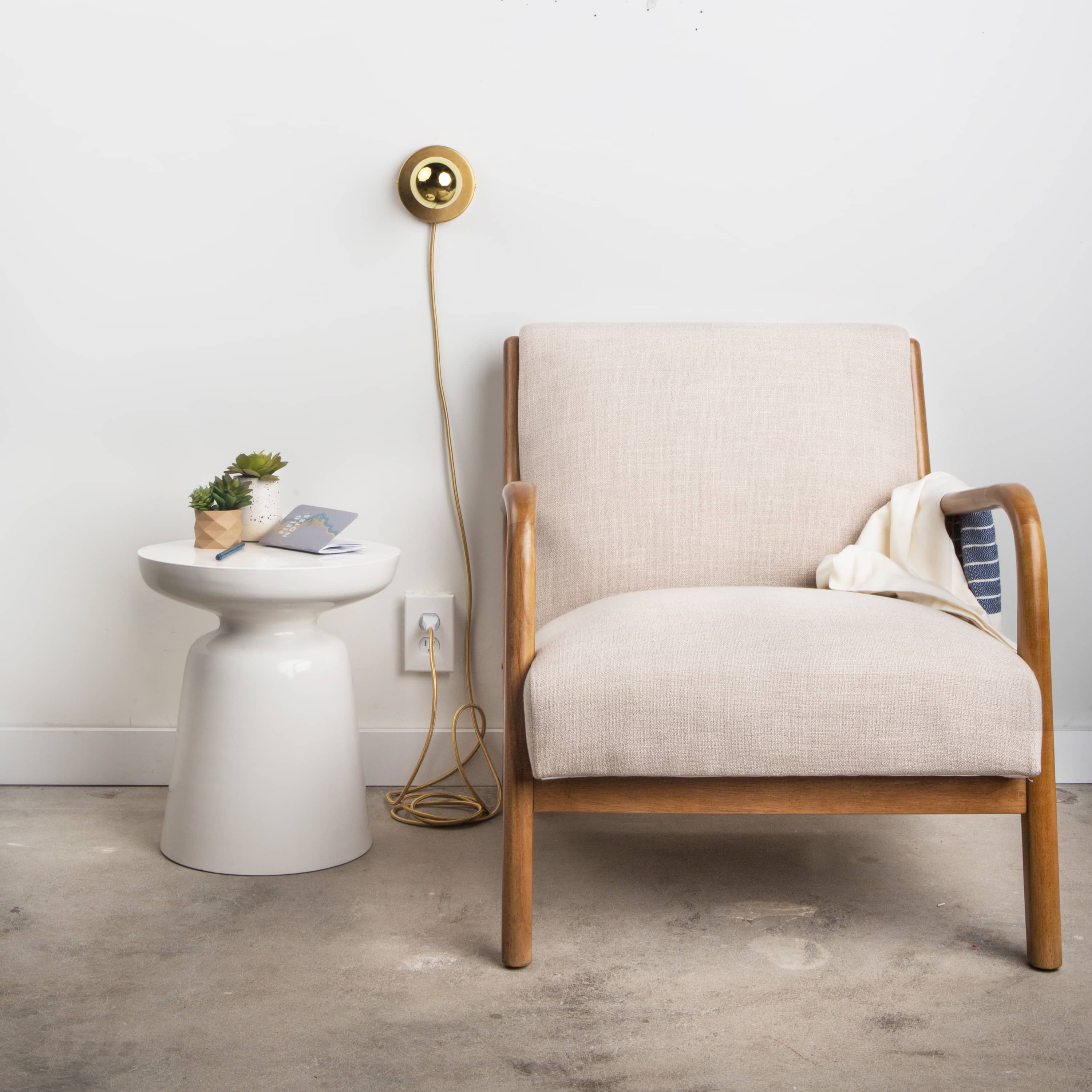 Room view with Button Plug-In sconce in Raw brass finish above a side table and chair. Pictured with a G25 gold mirrored bulb.