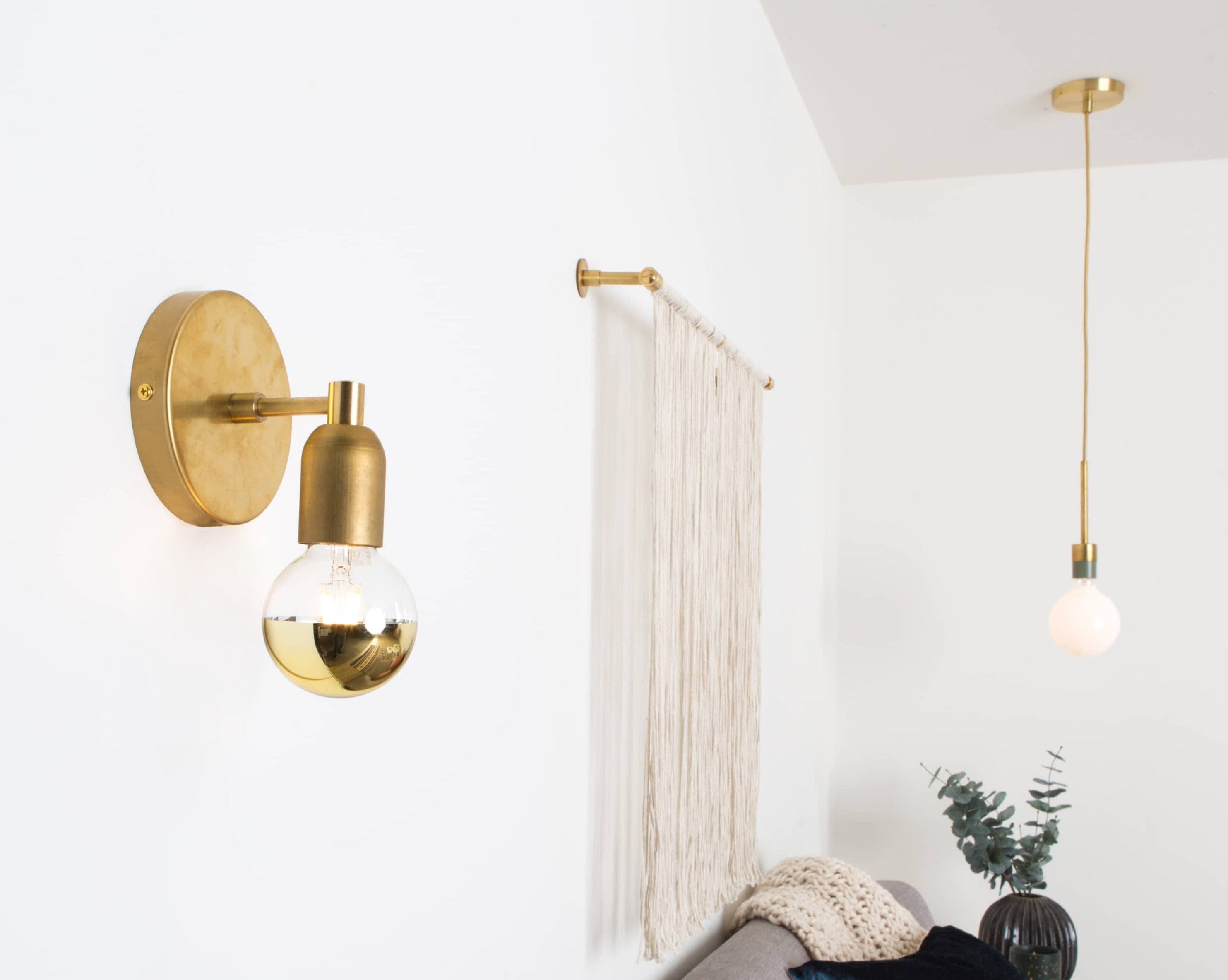 Junction Mini Solo Sconce in Raw Brass finish mounted on wall next to string art piece.