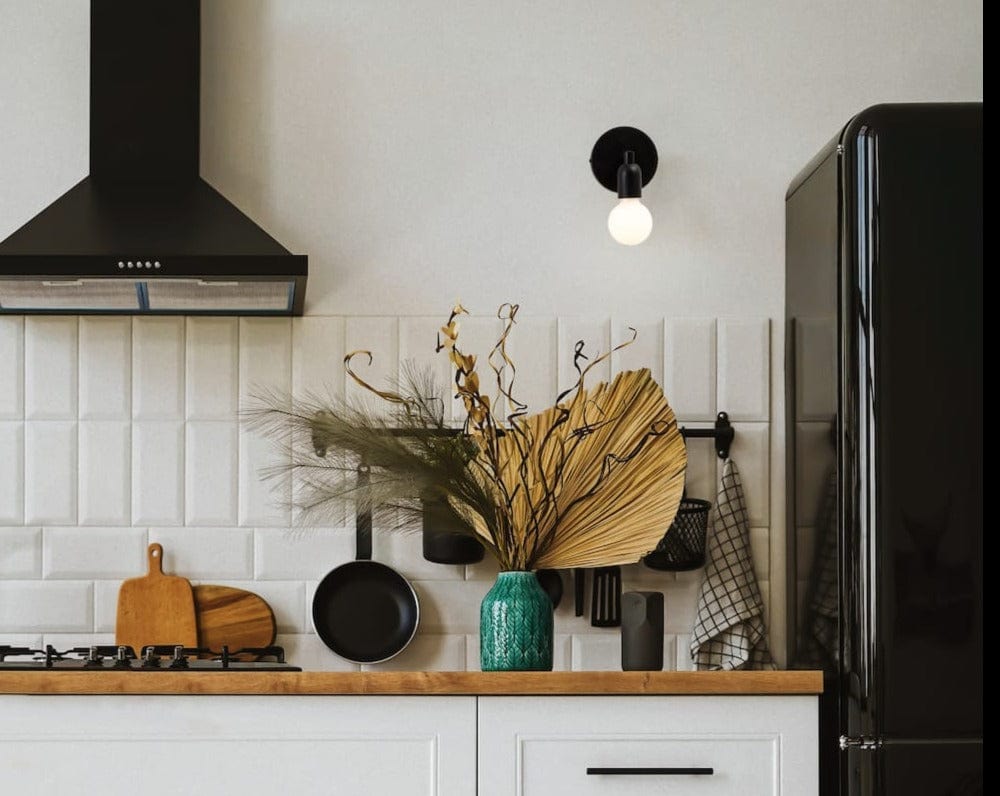 Room view of Junction Mini Solo Sconce in Matte Black finish. Mounted on wall in a kitchen above counter next to matching finish range hood