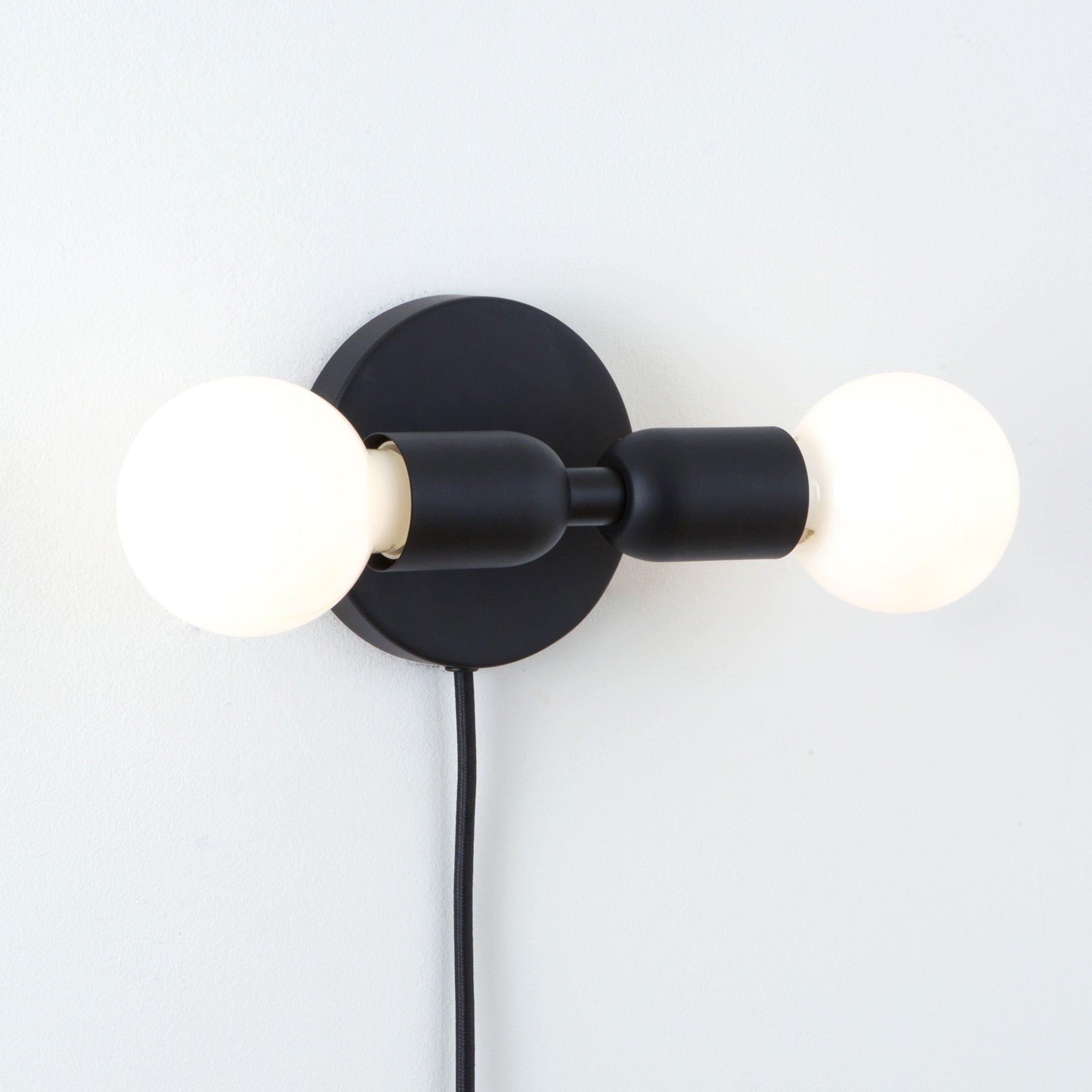 Junction Mini Duo Plug-In Sconce in Matte Black Finish. Pictured in horizontal orientation with G25 milk Glass bulbs