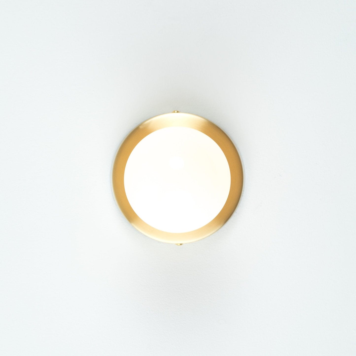 Button Light in Raw Brass finish. Pictured with a G40 milk glass light bulb. Straight on angle.