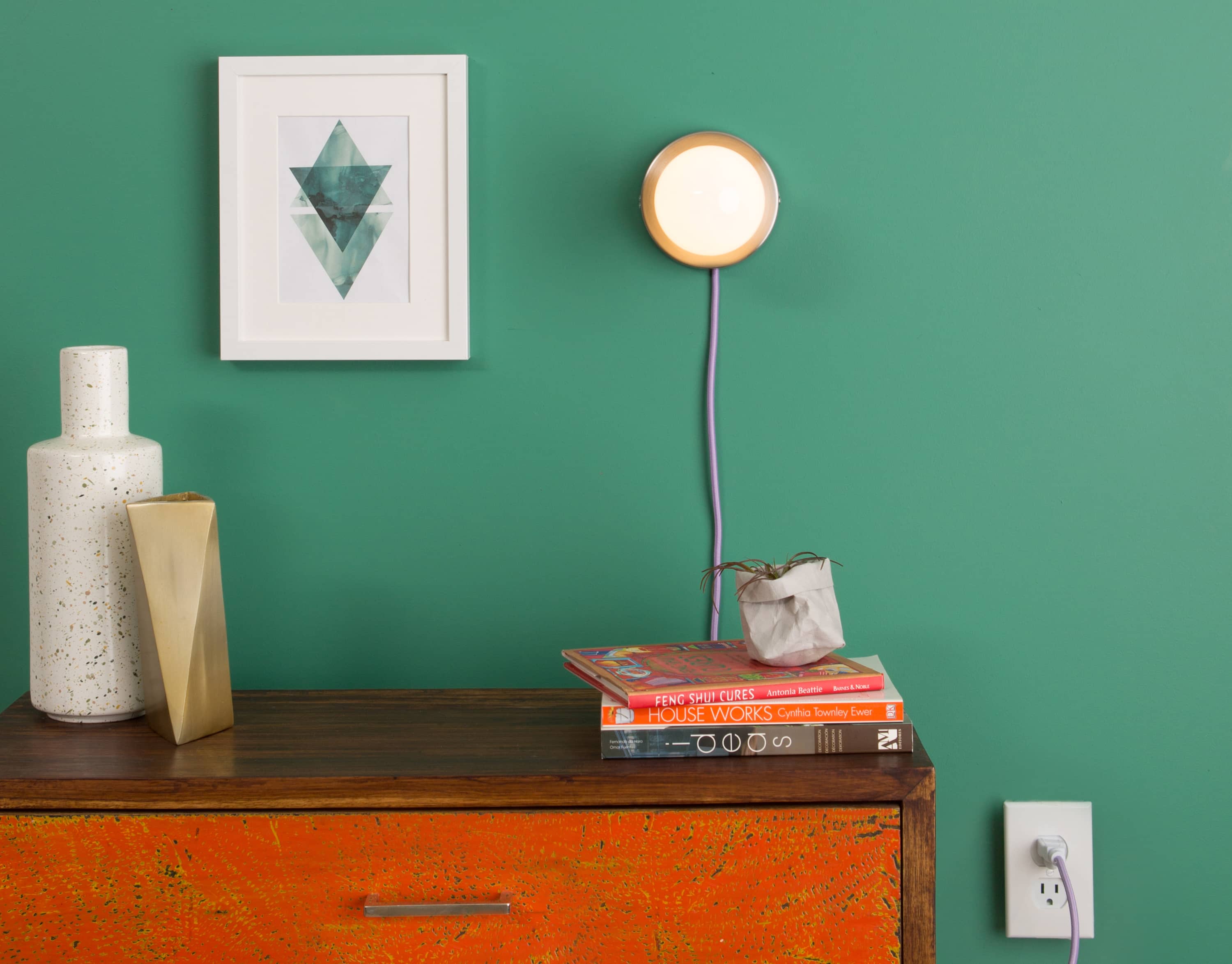 Room view photo of Button Plug-In Sconce in Raw Brass finish customized with a Lilac (lavender) colored power cord. Light fixture above console table mounted on a green wall